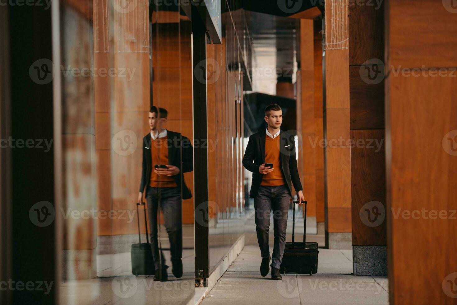 Going to airport terminal. Confident businessman traveler walking on city streets and pulling his suitcase drinking coffee and speaking on smartphone photo