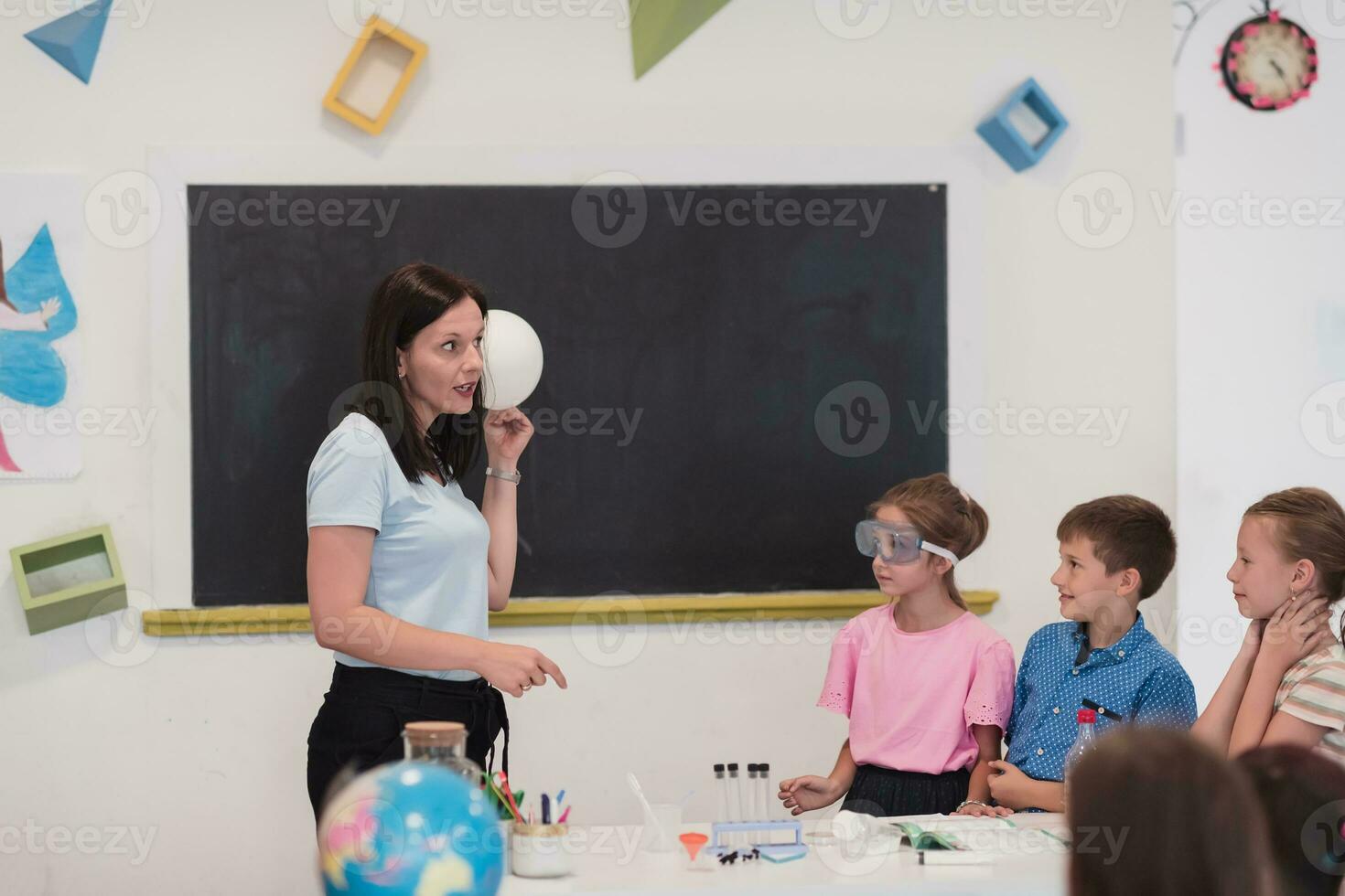 Elementary School Science Classroom Enthusiastic Teacher Explains Chemistry to Diverse Group of Children, Little Boy Mixes Chemicals in Beakers. Children Learn with Interest photo