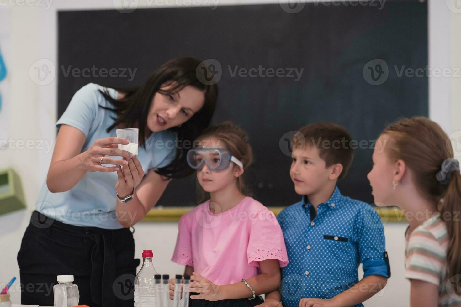 Elementary School Science Classroom Enthusiastic Teacher Explains Chemistry to Diverse Group of Children, Little Boy Mixes Chemicals in Beakers. Children Learn with Interest photo