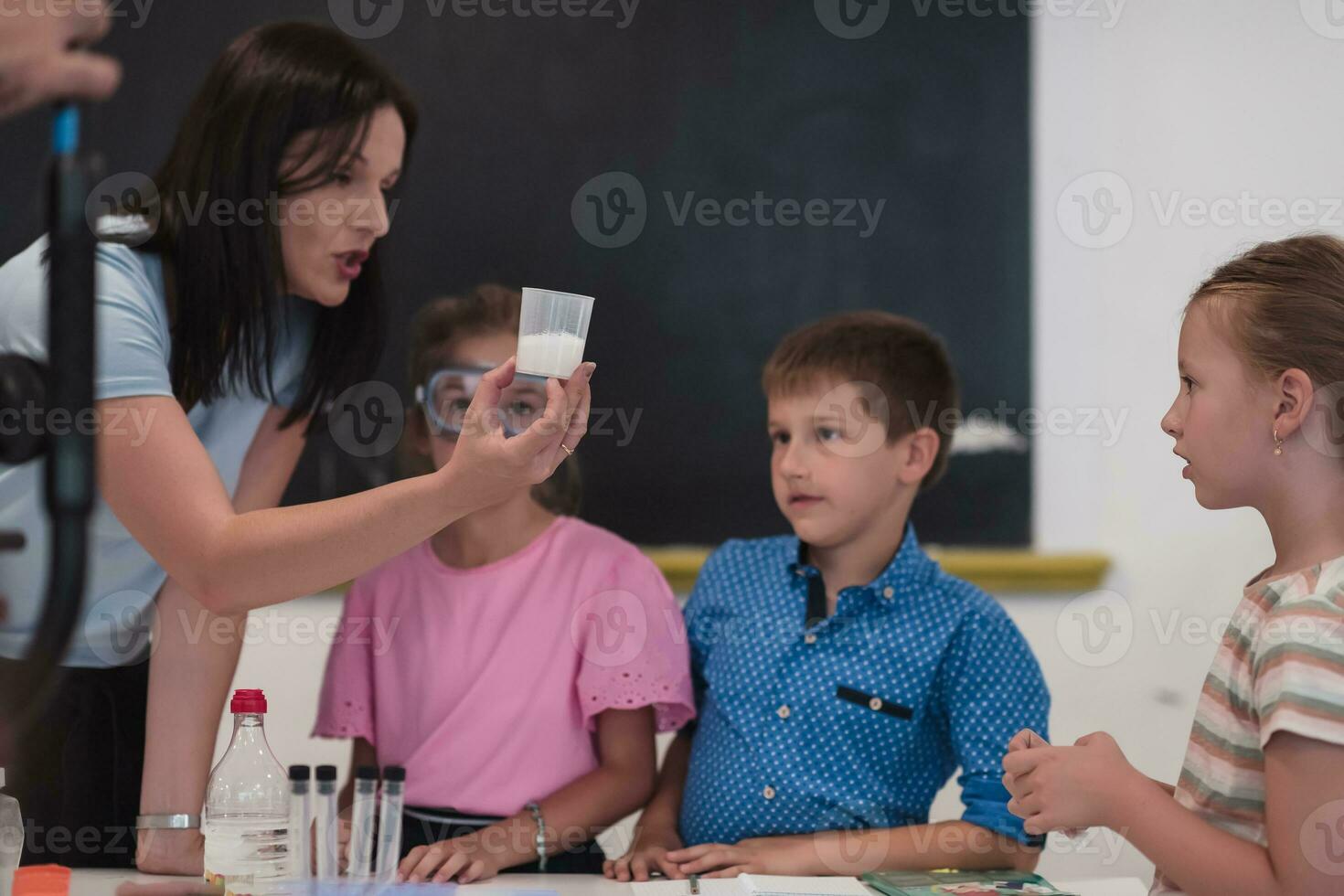 Elementary School Science Classroom Enthusiastic Teacher Explains Chemistry to Diverse Group of Children, Little Boy Mixes Chemicals in Beakers. Children Learn with Interest photo