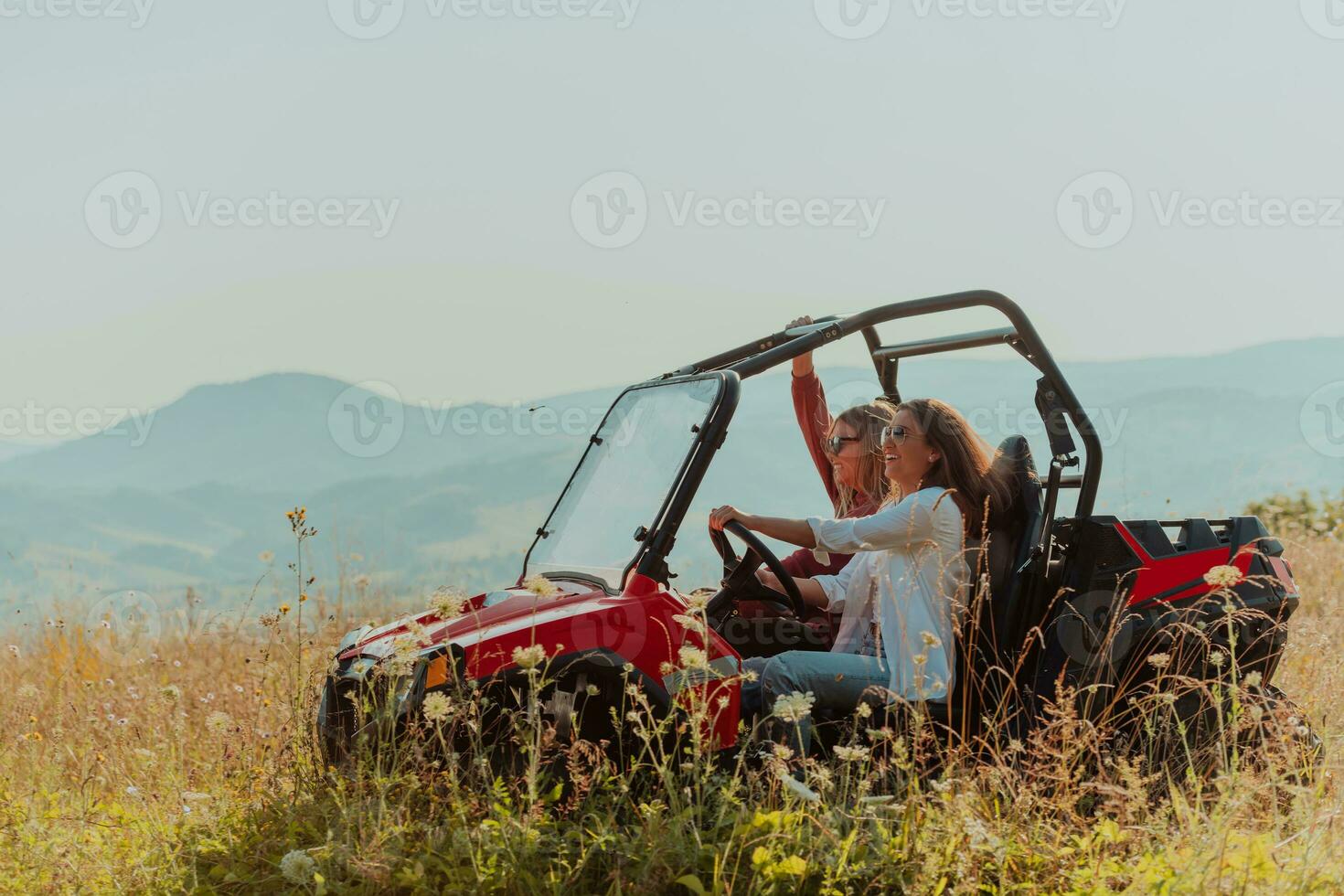 Two young happy excited women enjoying beautiful sunny day while driving a off road buggy car on mountain nature photo