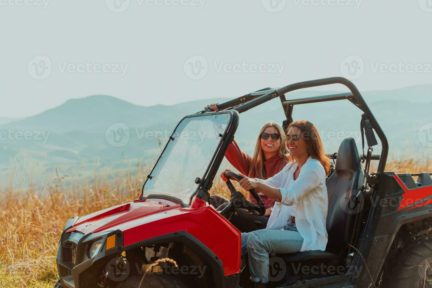 Two young happy excited women enjoying beautiful sunny day while driving a off road buggy car on mountain nature photo