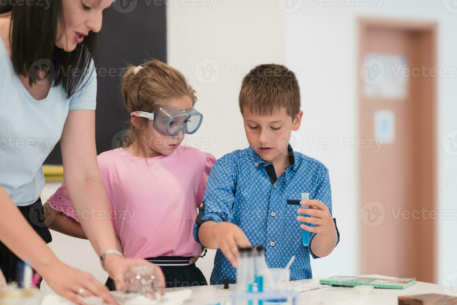 Elementary School Science Classroom Enthusiastic Teacher Explains Chemistry to Diverse Group of Children, Little Boy Mixes Chemicals in Beakers. Children Learn with Interest photo