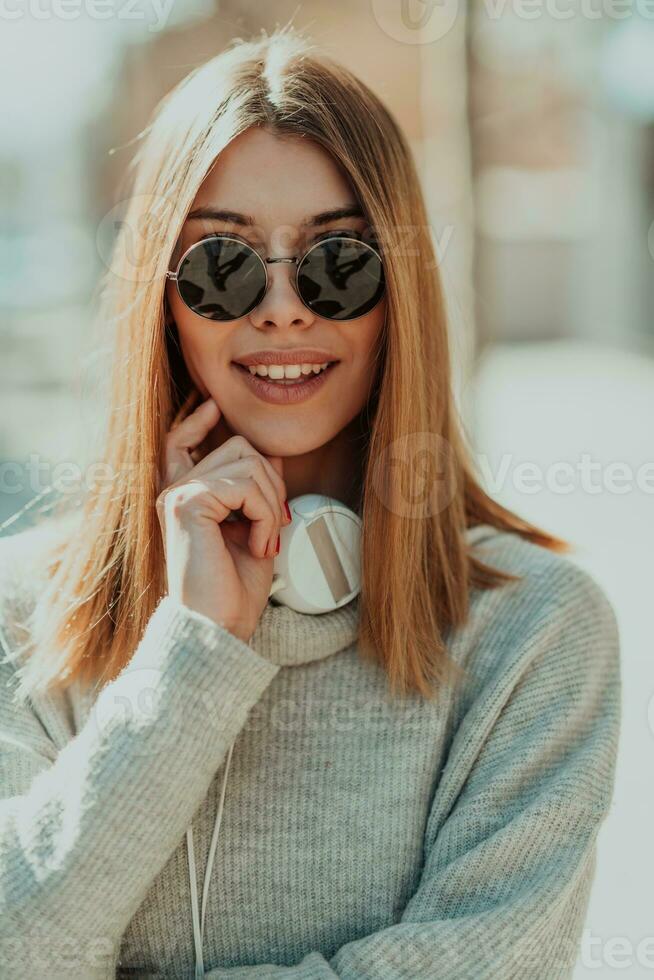 a modern girl with sunglasses walking down the street listens to music in headphones. photo