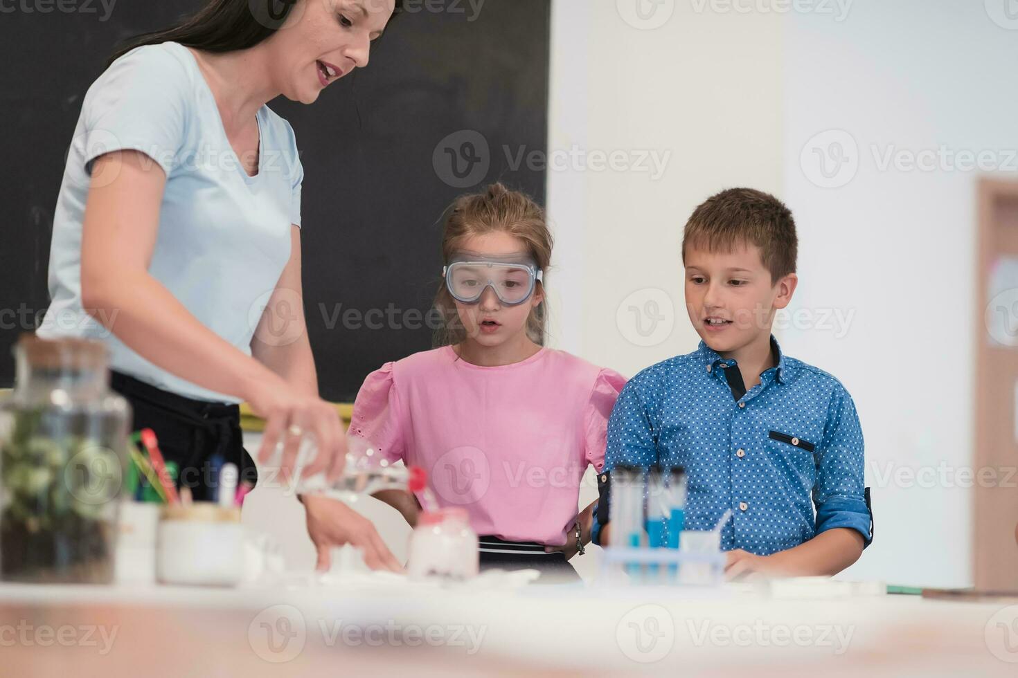 Elementary School Science Classroom Enthusiastic Teacher Explains Chemistry to Diverse Group of Children, Little Boy Mixes Chemicals in Beakers. Children Learn with Interest photo