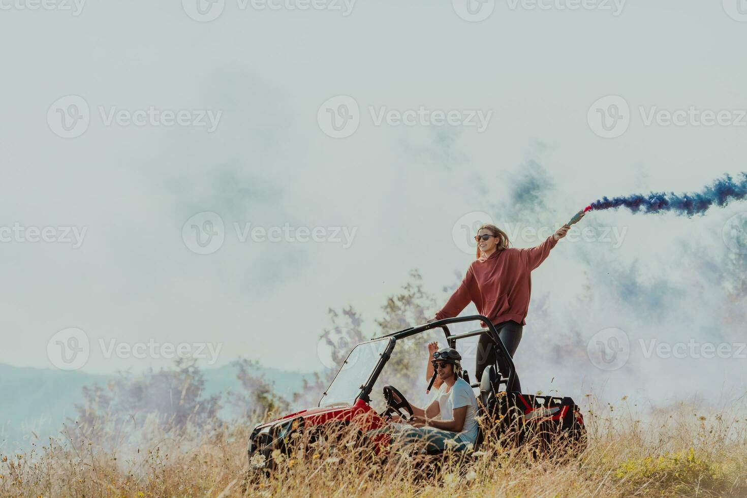 Group of young happy excited people having fun enjoying beautiful sunny day holding colorful torches while driving a off road buggy car on mountain nature. photo