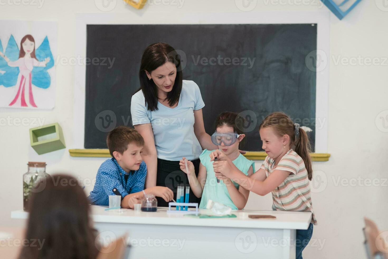 Elementary School Science Classroom Enthusiastic Teacher Explains Chemistry to Diverse Group of Children, Little Boy Mixes Chemicals in Beakers. Children Learn with Interest photo