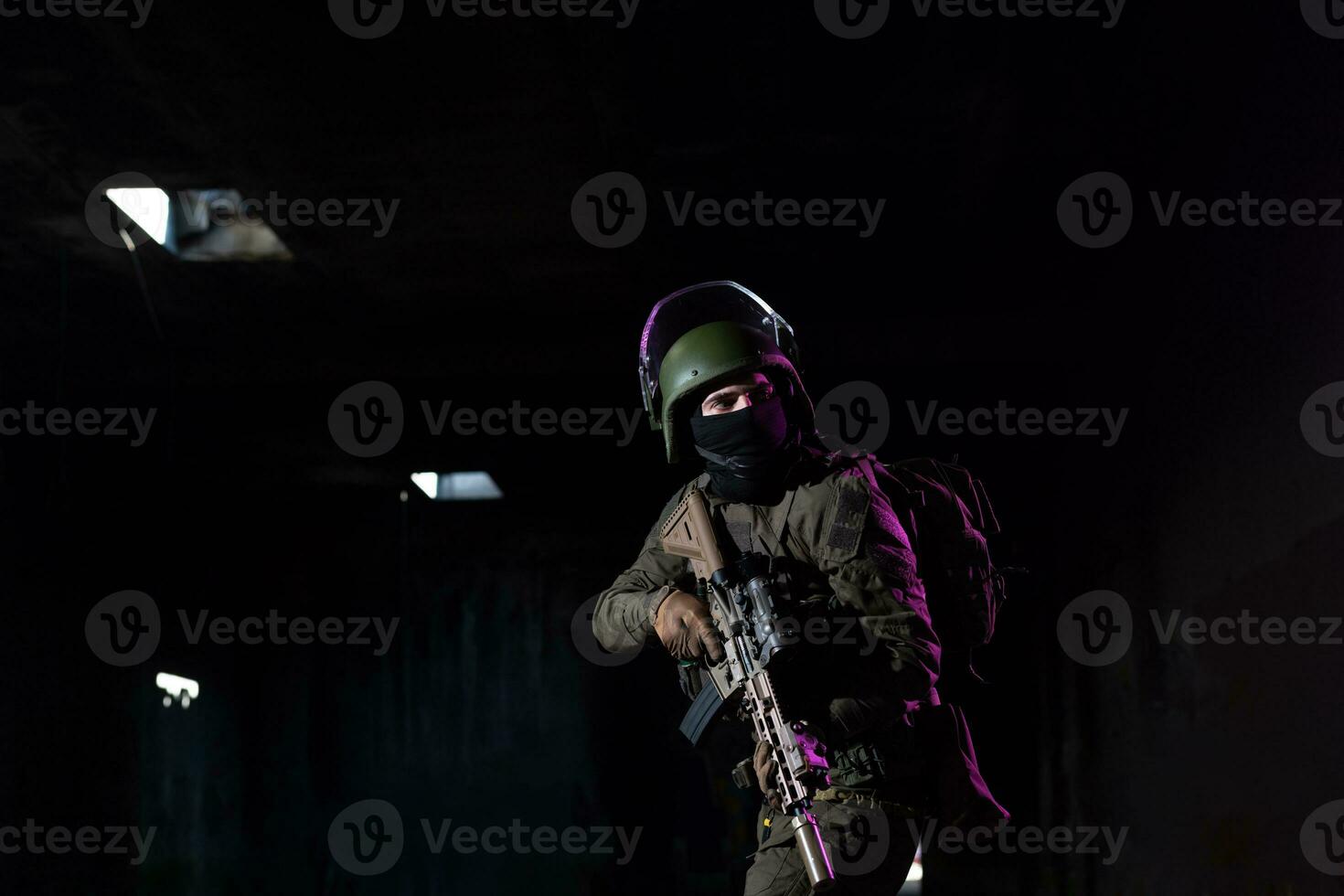 Army soldier in Combat Uniforms with an assault rifle and combat helmet night mission dark background. Blue and purple gel light effect. photo