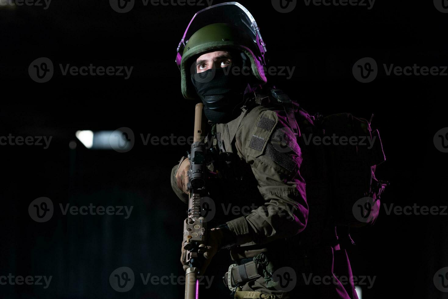 Army soldier in Combat Uniforms with an assault rifle and combat helmet night mission dark background. Blue and purple gel light effect. photo