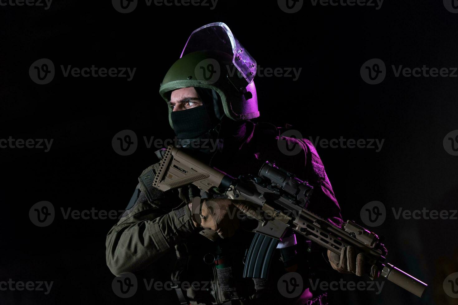 Army soldier in Combat Uniforms with an assault rifle and combat helmet night mission dark background. Blue and purple gel light effect. photo