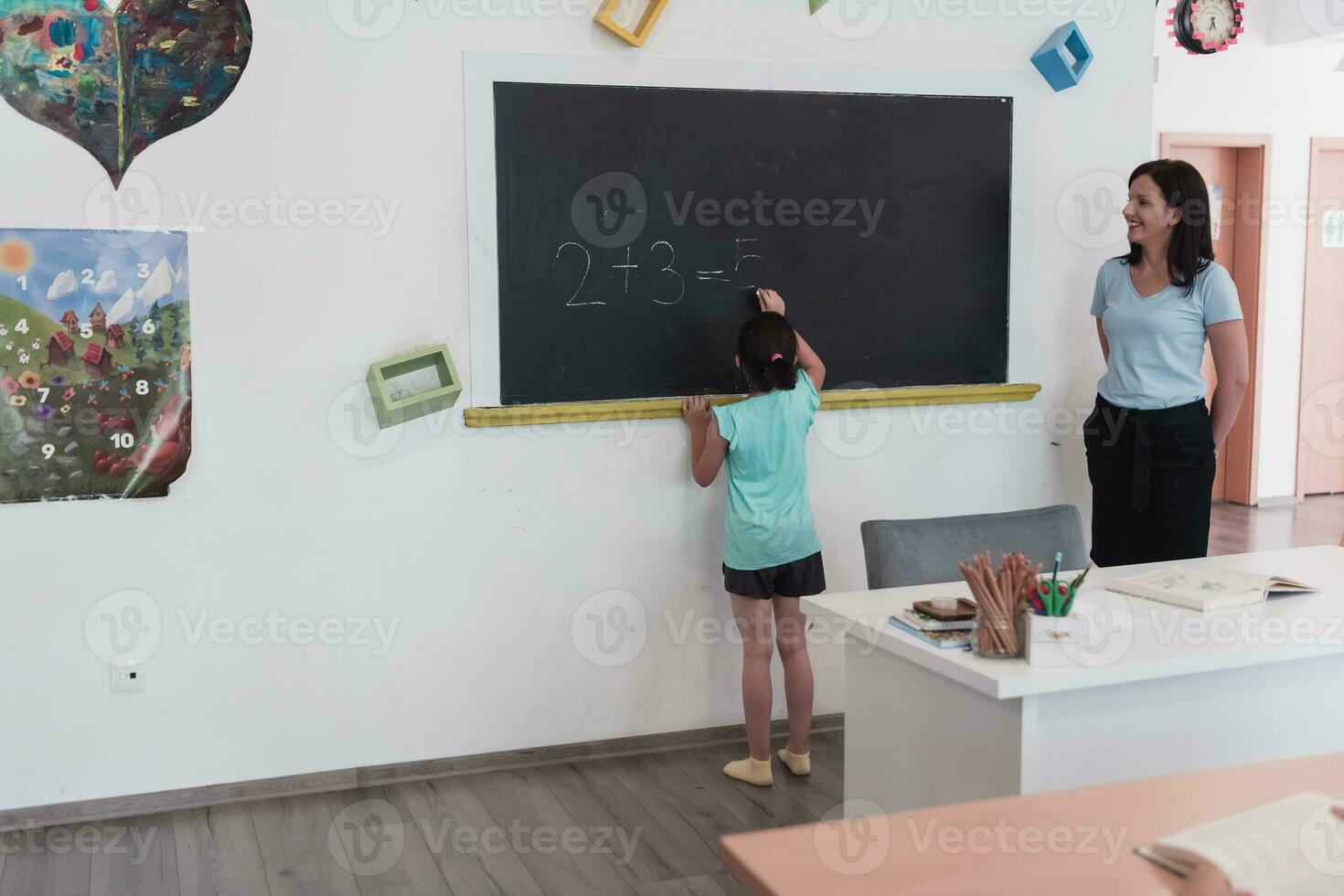 Elementary school. The female teacher helping the child student while writing the answer on the chalkboard. photo