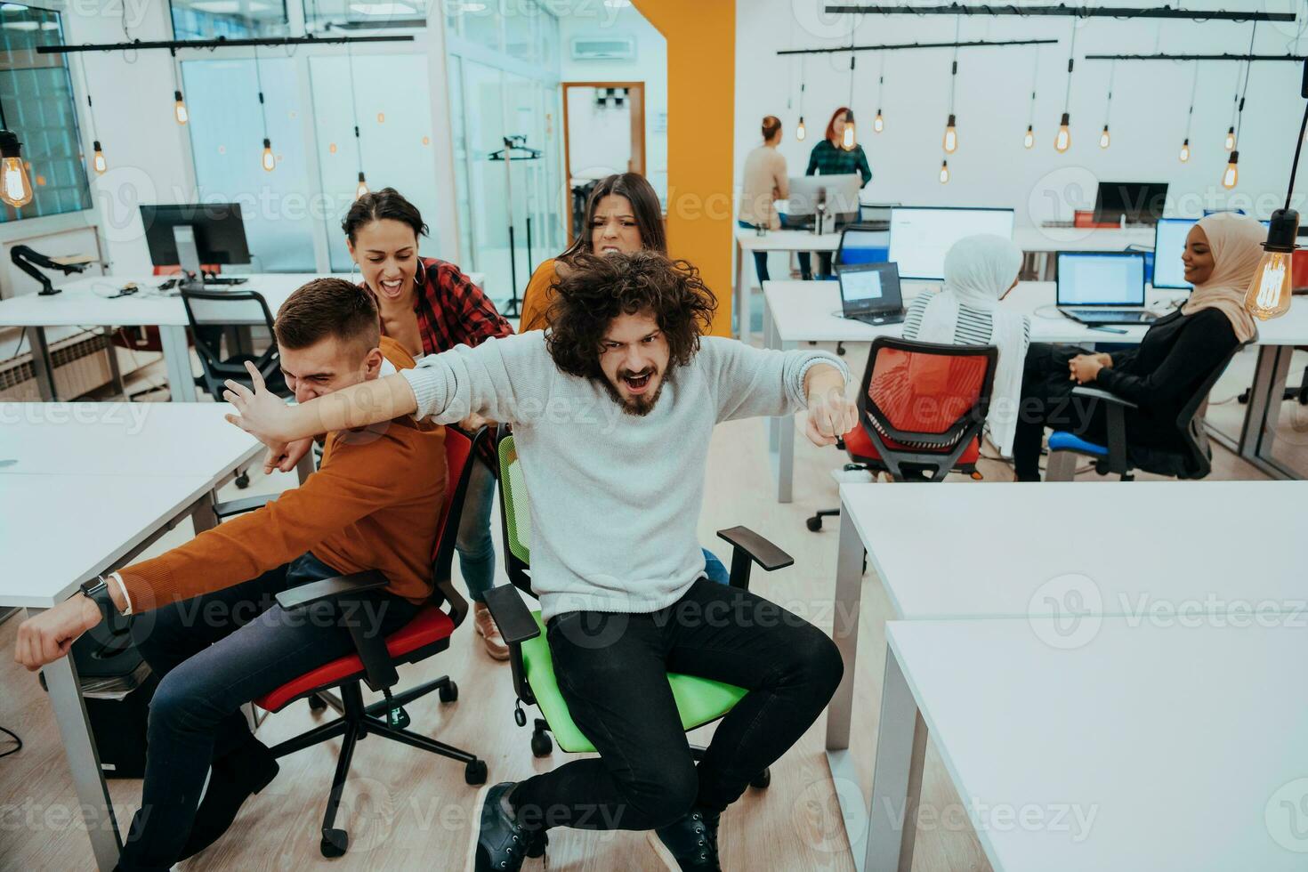 Team building and office fun. Young cheerful businesspeople in smart casual wear having fun while racing on office chairs and smiling. photo