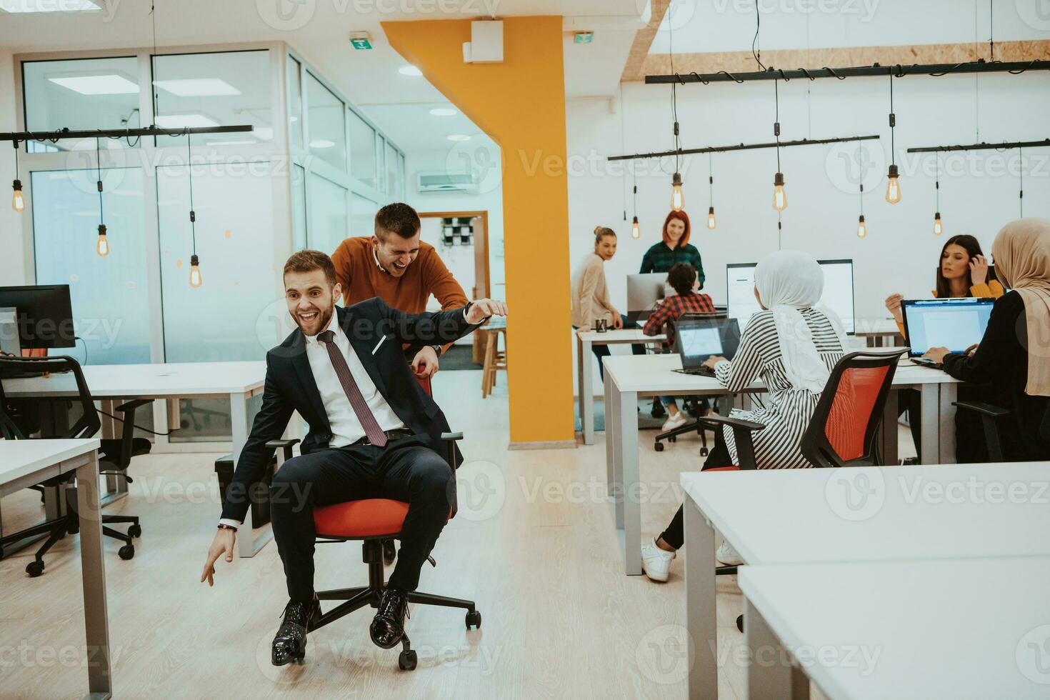 Team building and office fun. Young cheerful businesspeople in smart casual wear having fun while racing on office chairs and smiling. photo