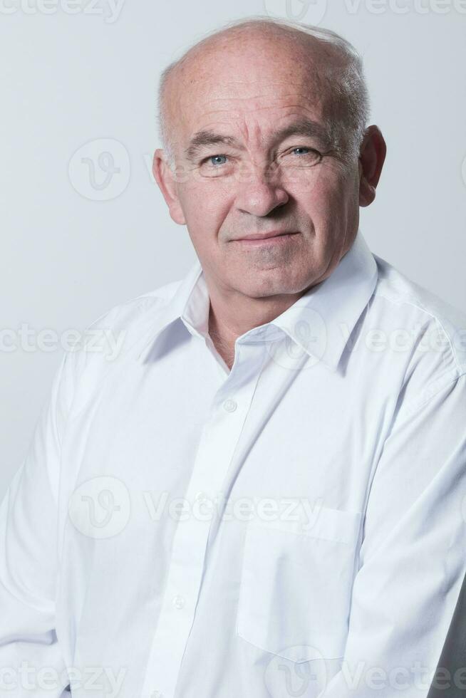 retrato de un más viejo hombre vistiendo un blanco camisa en un gris antecedentes. un sano antiguo hombre mira a un cámara aislado terminado un gris pared. un más viejo hombre sonrisas a el cámara, un contento antiguo hombre. foto