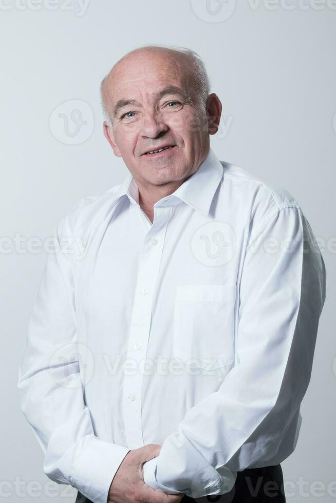 retrato de un más viejo hombre vistiendo un blanco camisa en un gris antecedentes. un sano antiguo hombre mira a un cámara aislado terminado un gris pared. un más viejo hombre sonrisas a el cámara, un contento antiguo hombre. foto