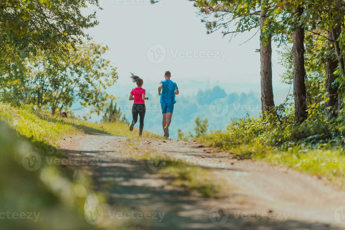 Couple enjoying in a healthy lifestyle while jogging on a country road through the beautiful sunny forest, exercise and fitness concept photo