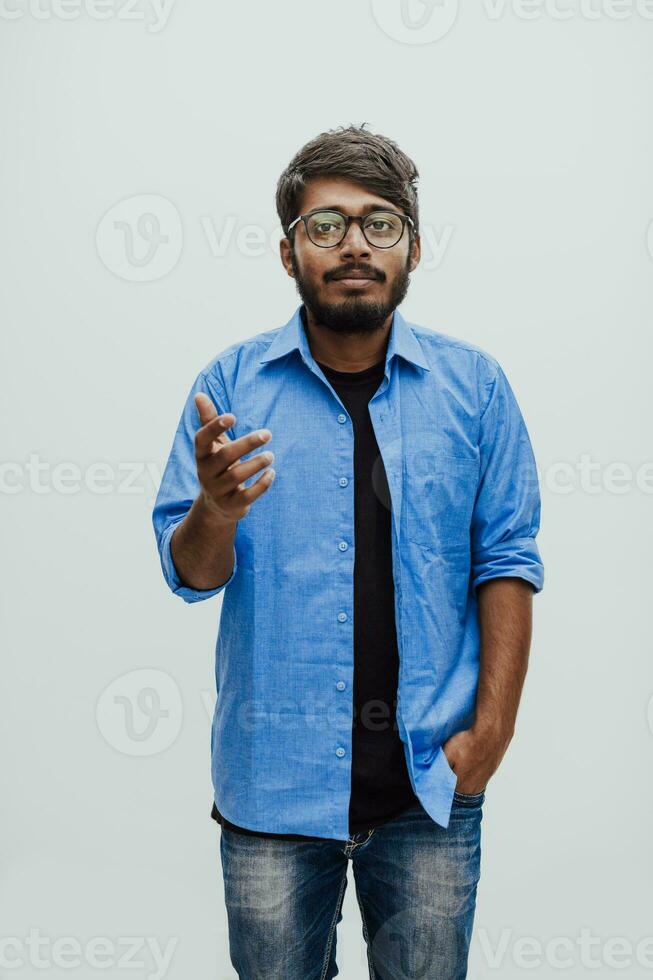 Indian smiling young man with blue shirt and glasses posing on gray background photo