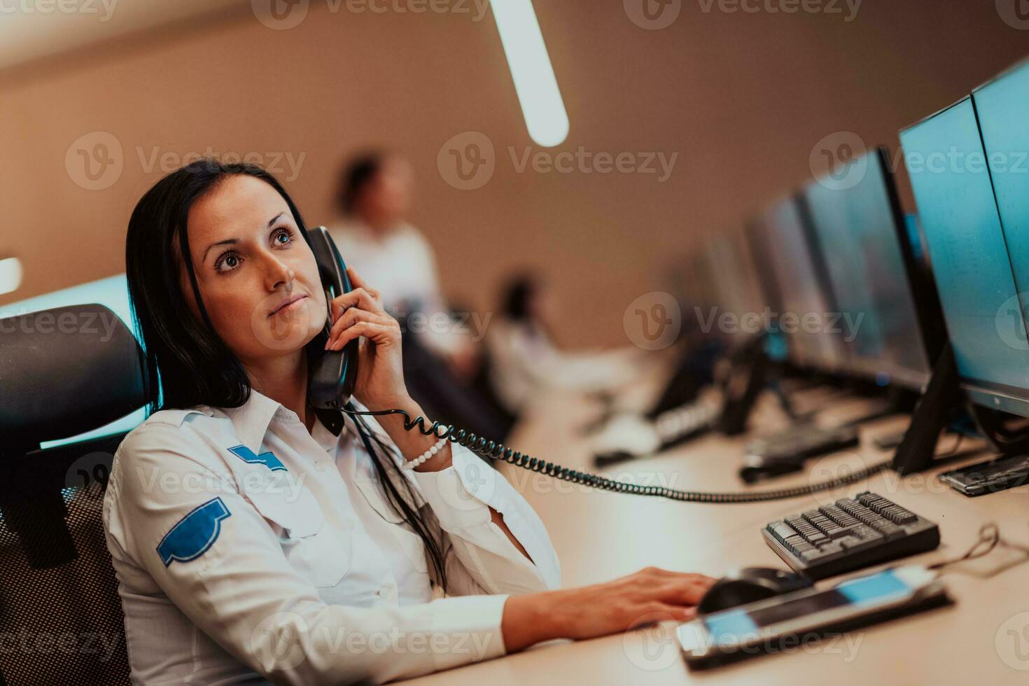 hembra seguridad Guardia operador hablando en el teléfono mientras trabajando a puesto de trabajo con múltiple muestra seguridad guardias trabajando en múltiple monitores foto