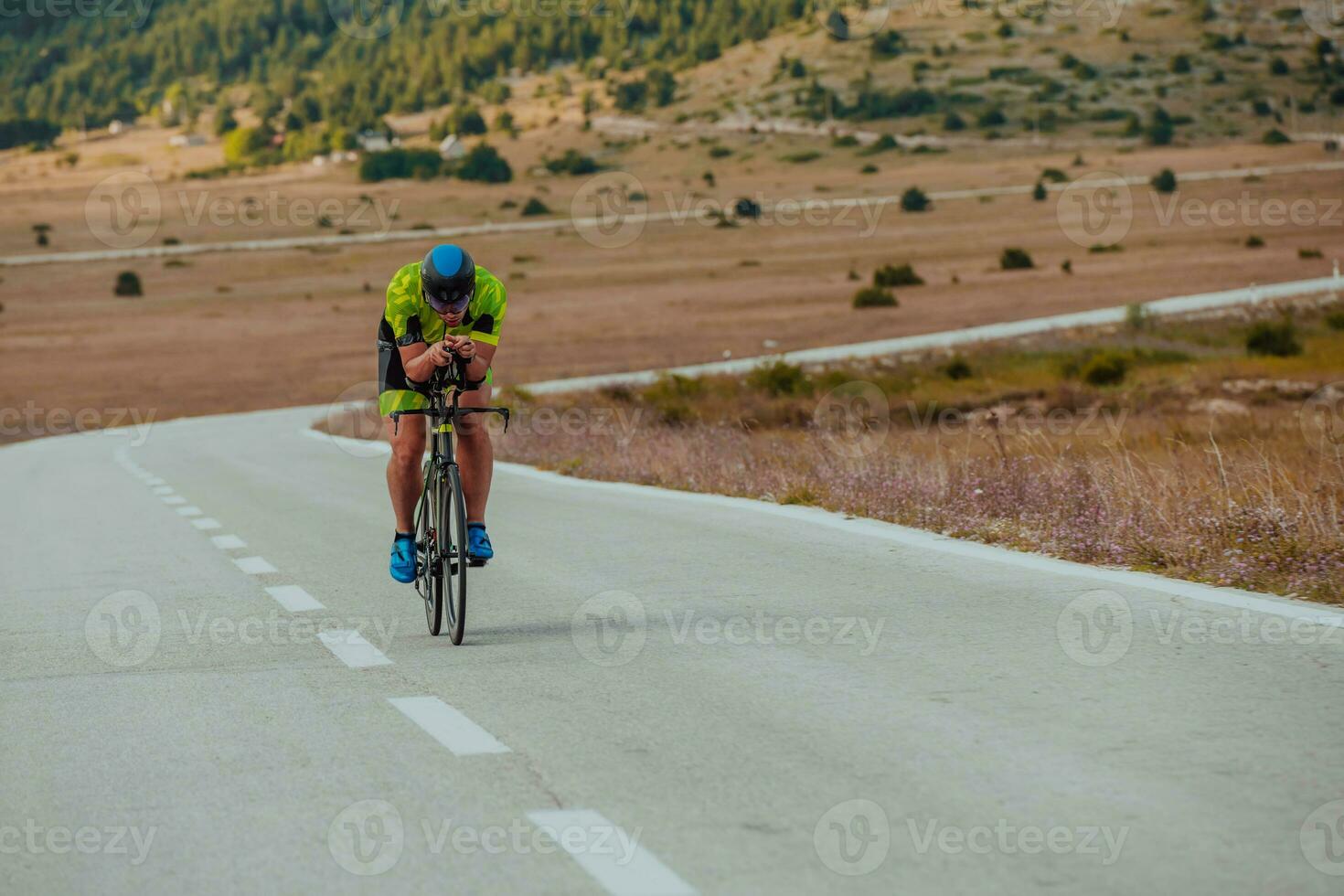 Full length portrait of an active triathlete in sportswear and with a protective helmet riding a bicycle. Selective focus photo