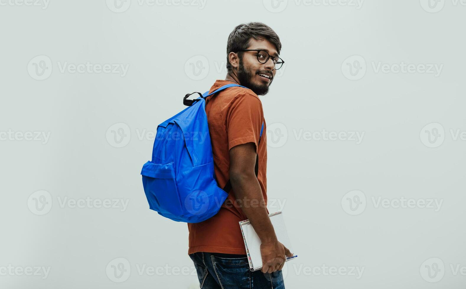 Indian student with blue backpack, glasses and notebook posing on gray background. The concept of education and schooling. Time to go back to school photo