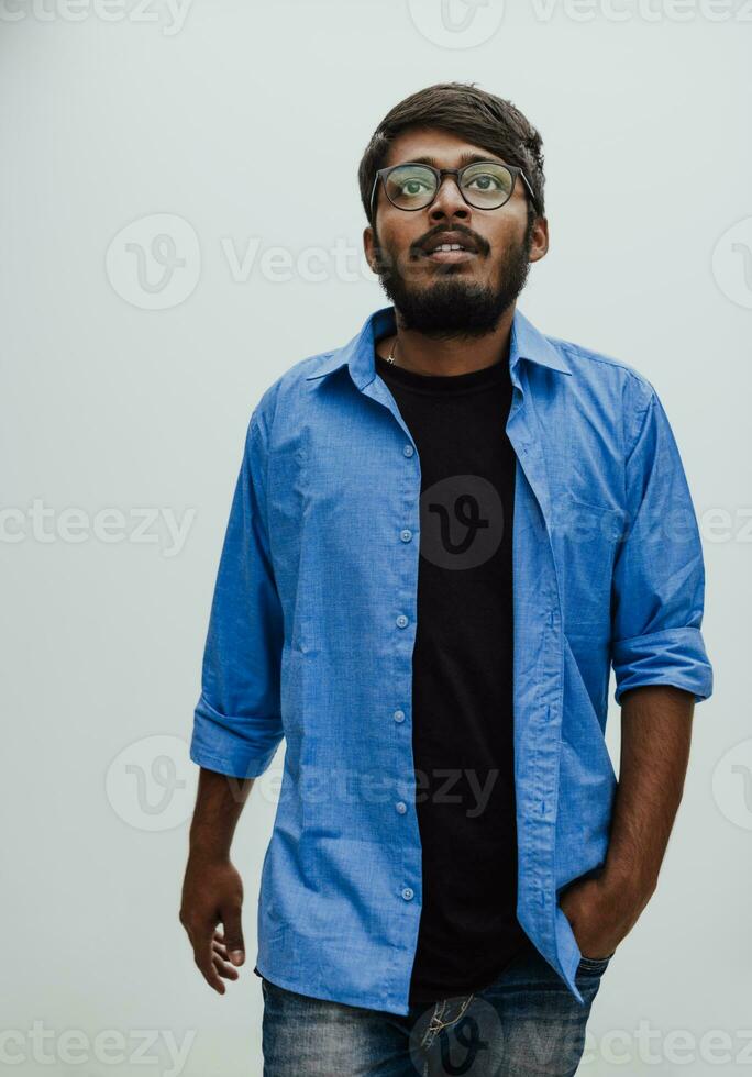 Indian smiling young man with blue shirt and glasses posing on gray background photo