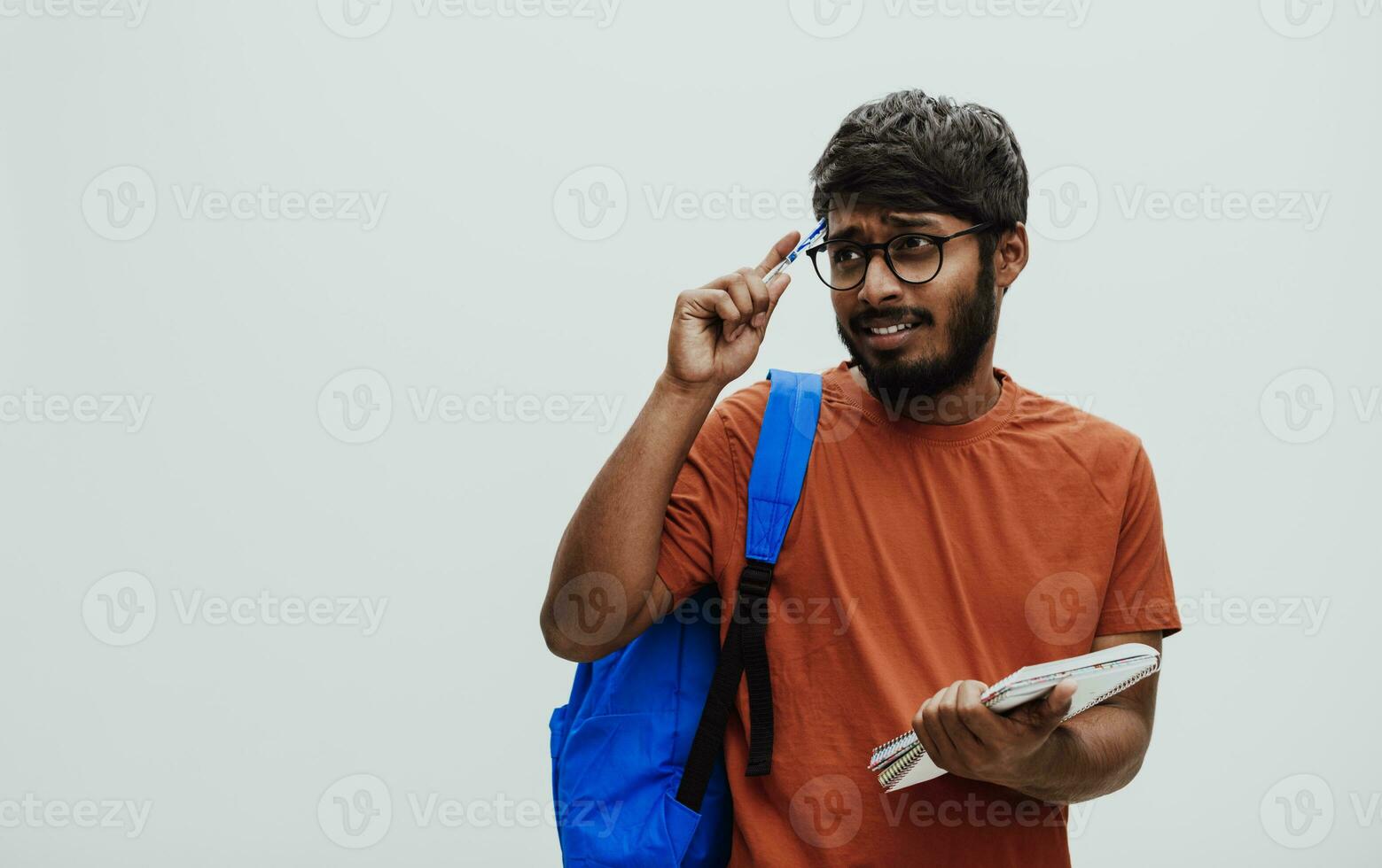 Confused indian student with blue backpack, glasses and notebook posing on gray background. The concept of education and schooling. Time to go back to school photo