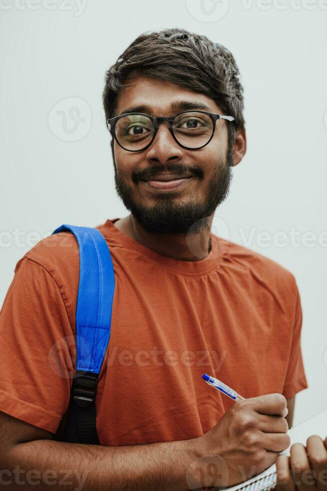 Indian student with blue backpack, glasses and notebook posing on gray background. The concept of education and schooling. Time to go back to school photo