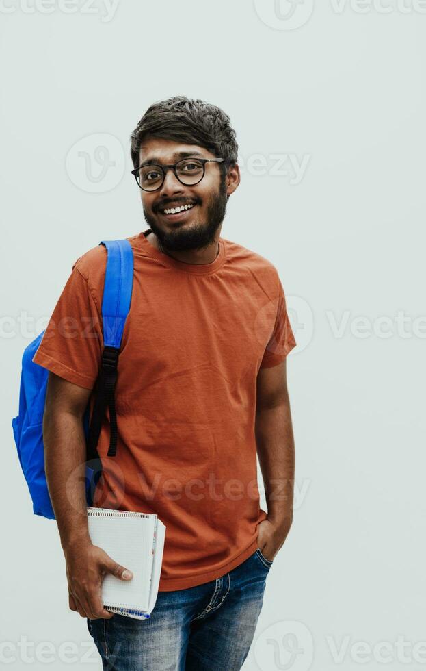 indio estudiante con azul mochila, lentes y cuaderno posando en gris antecedentes. el concepto de educación y enseñanza. hora a Vamos espalda a colegio foto