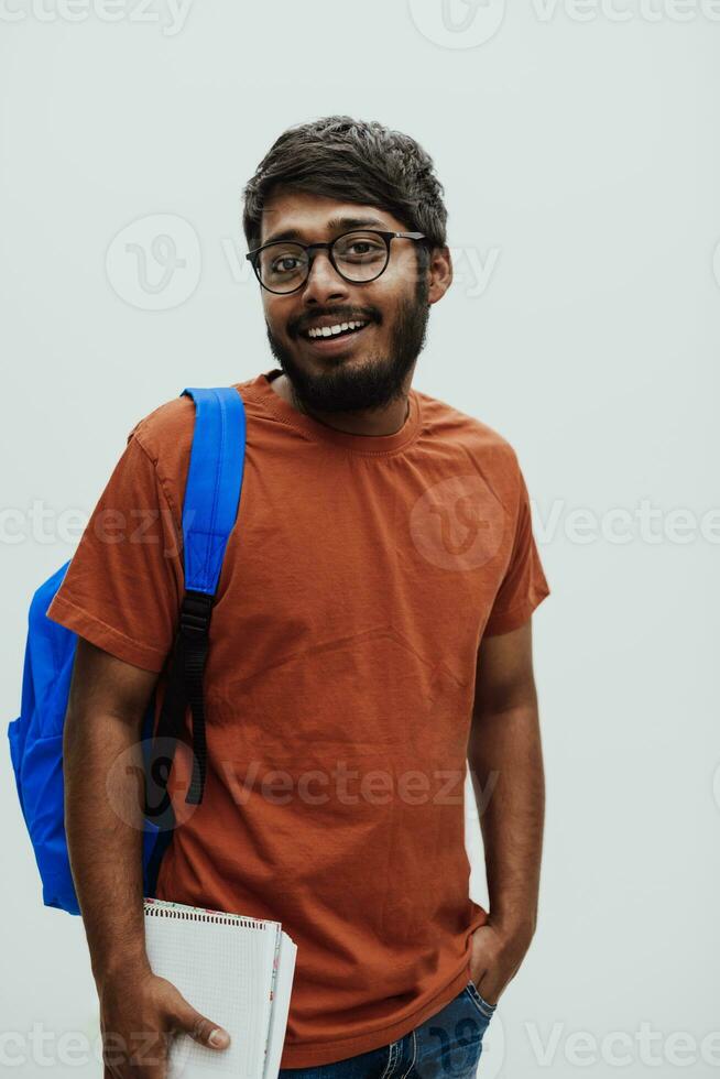 Indian student with blue backpack, glasses and notebook posing on gray background. The concept of education and schooling. Time to go back to school photo