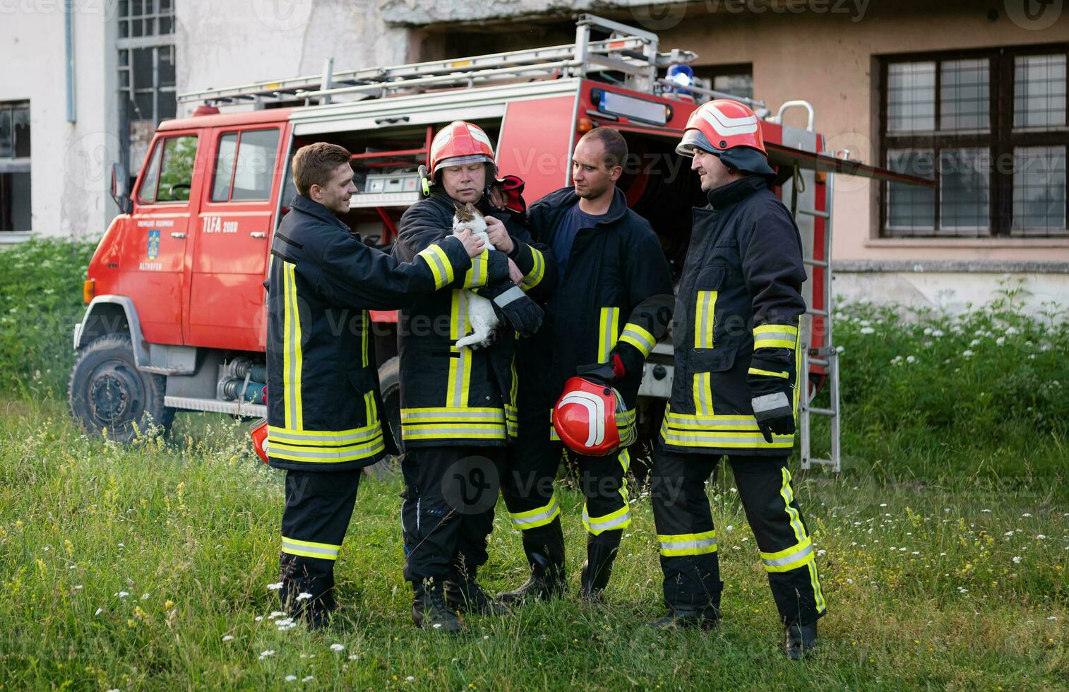 firefighters group in a protective suit and red helmet holds saved cat in his arms. Firefighter in fire fighting operation. photo