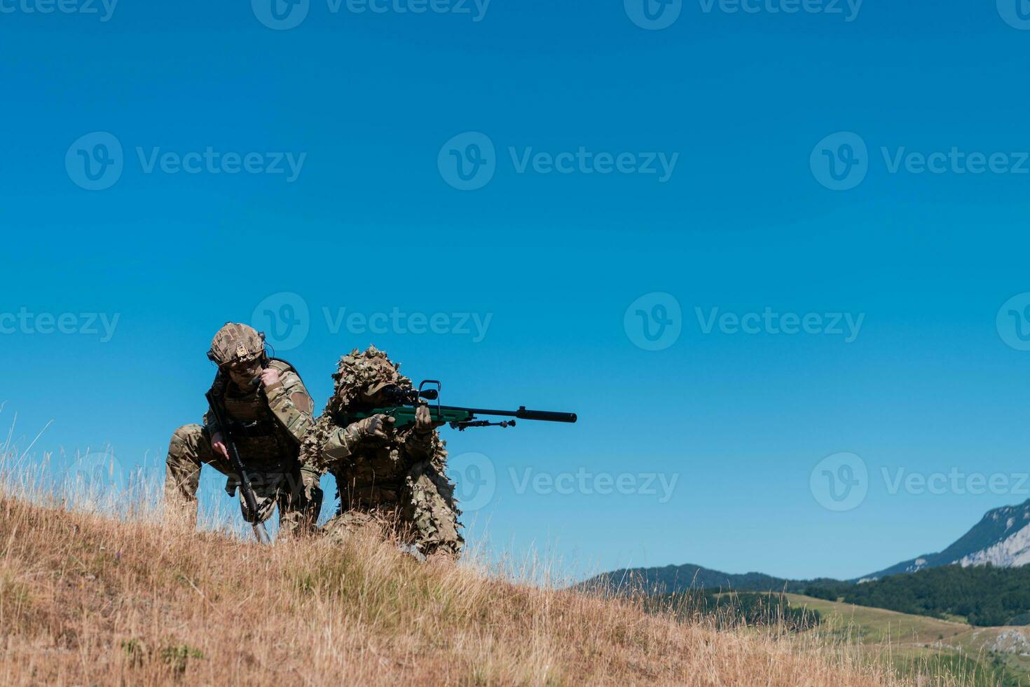 A sniper team squad of soldiers is going undercover. Sniper assistant and team leader walking and aiming in nature with yellow grass and blue sky. Tactical camouflage uniform. photo