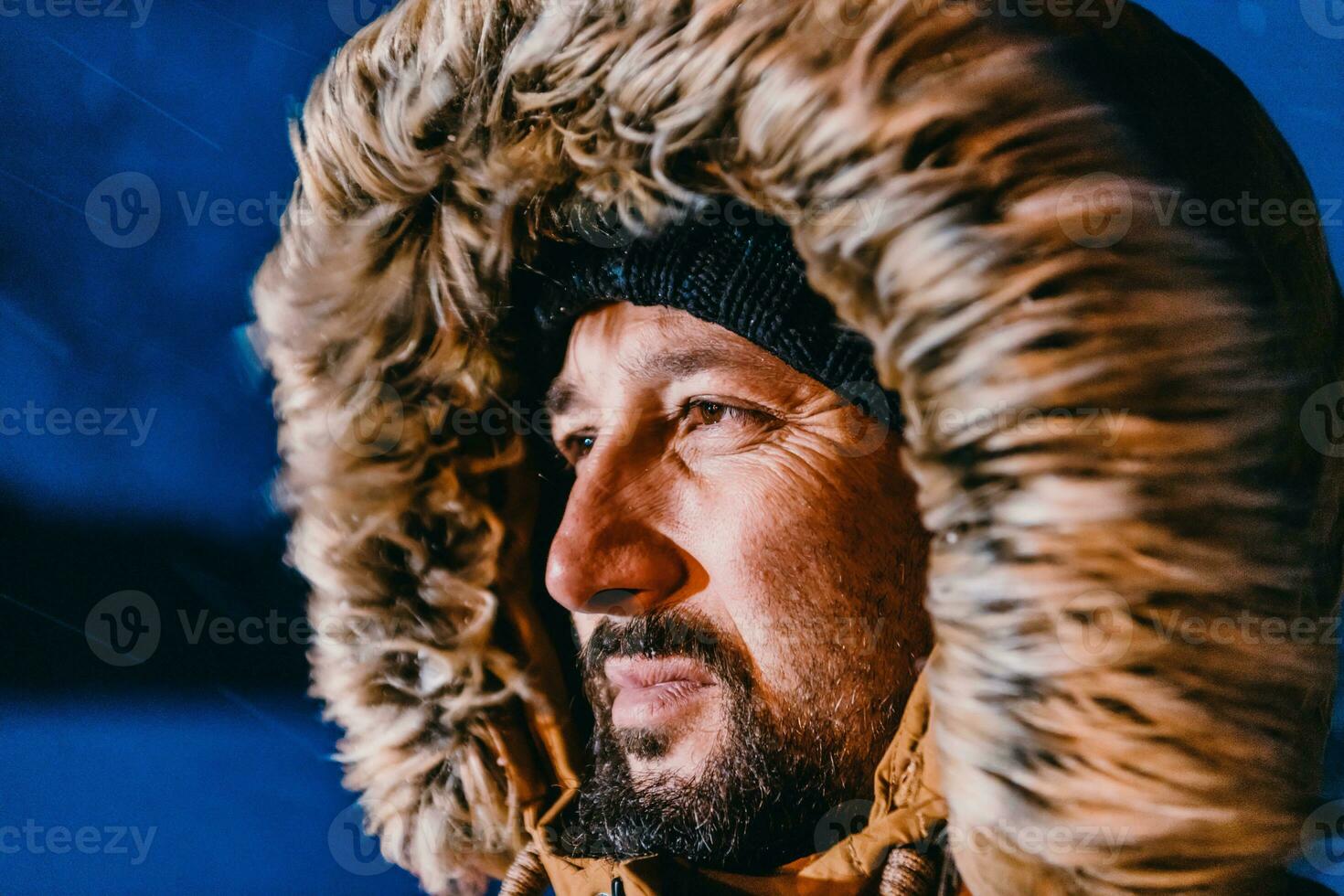 Head shot of a man in a cold snowy area wearing a thick brown winter jacket, snow goggles and gloves on a cold Scandinavian night. Life in the cold regions of the country. photo