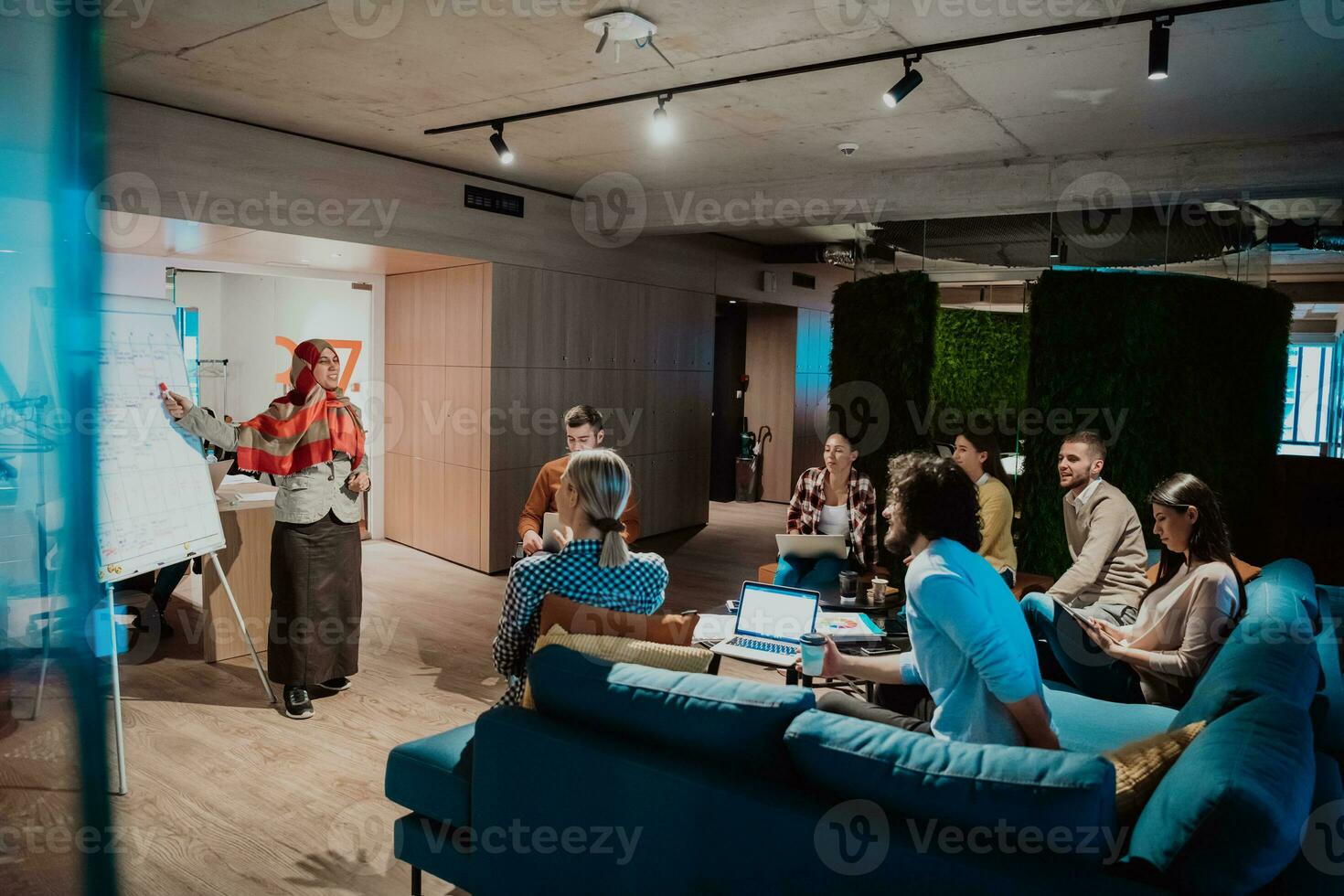 An older Muslim businesswoman presents a project to a young diverse team of people in a modern office photo