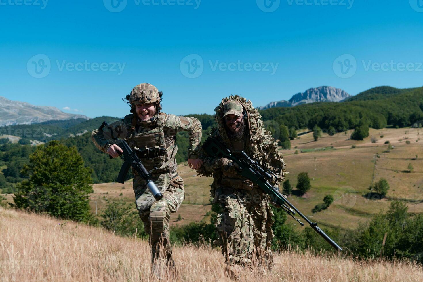 A sniper team squad of soldiers is going undercover. Sniper assistant and team leader walking and aiming in nature with yellow grass and blue sky. Tactical camouflage uniform. photo