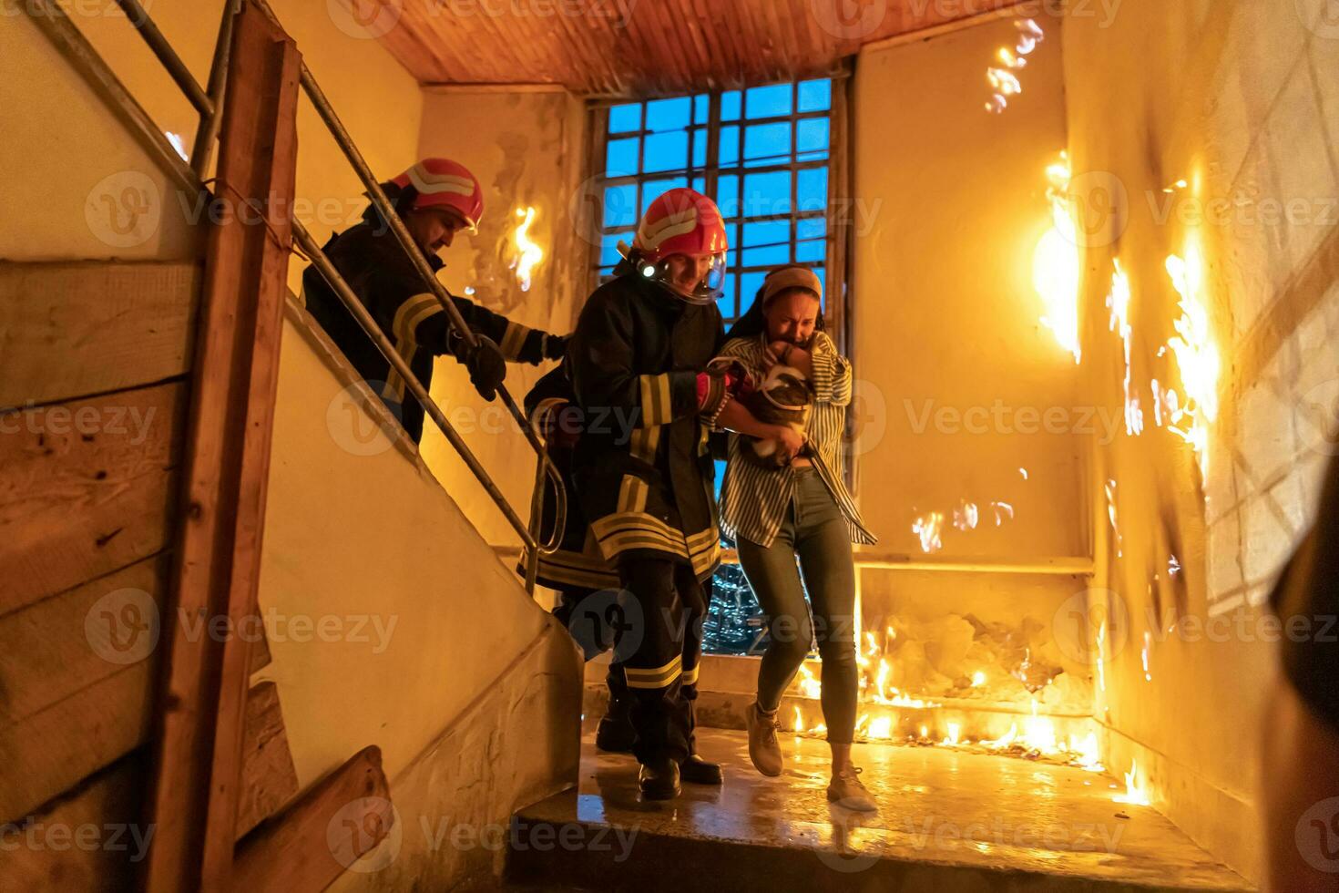 Brave Fireman Descends Stairs of a Burning Building and Holds Saved Girl in His Arms. Open fire and one Firefighter in the Background. photo