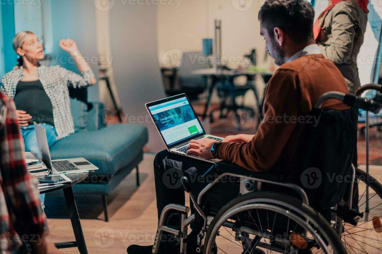 A businessman in a wheelchair in a modern coworking office space working on laptop. photo