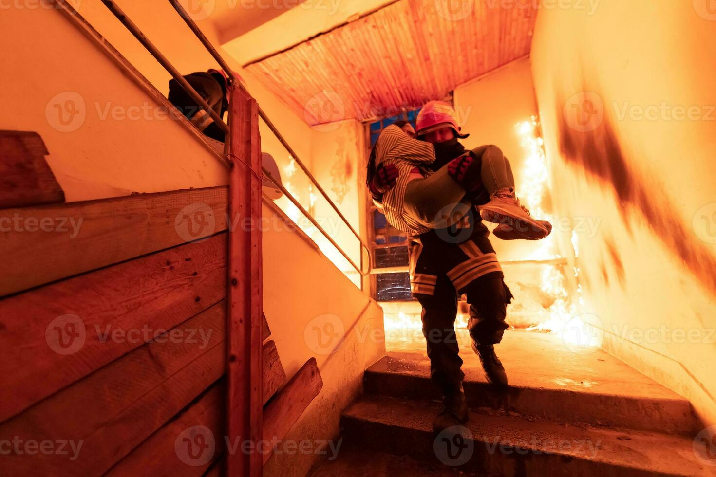 valiente bombero desciende escalera de un ardiente edificio y sostiene salvado niña en su brazos. abierto fuego y uno bombero en el antecedentes. foto