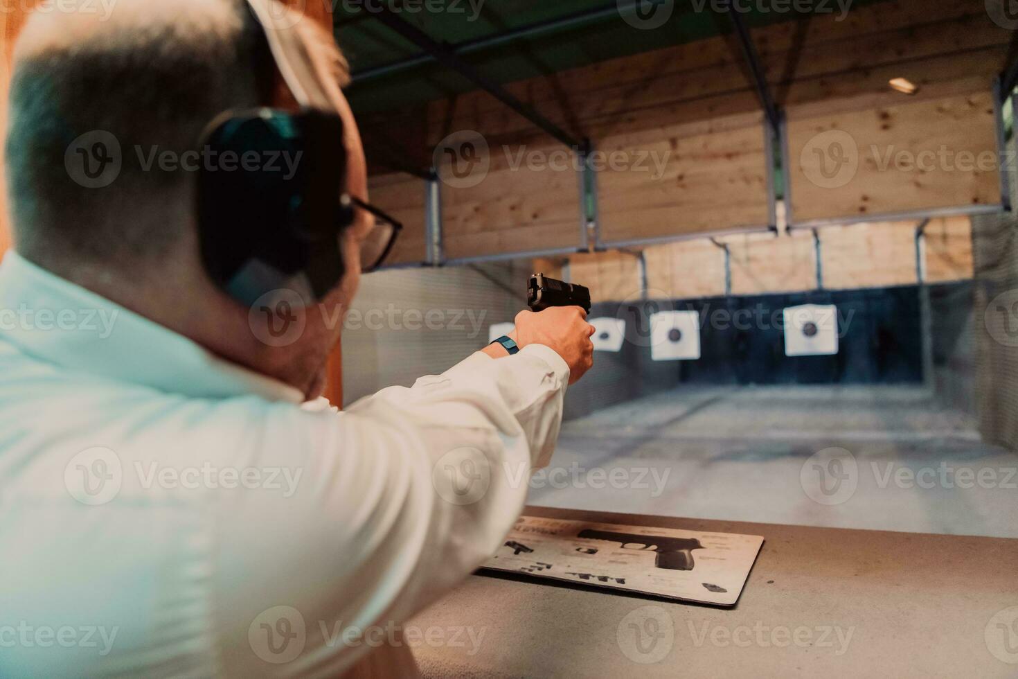 A man practices shooting a pistol in a shooting range while wearing protective headphones photo
