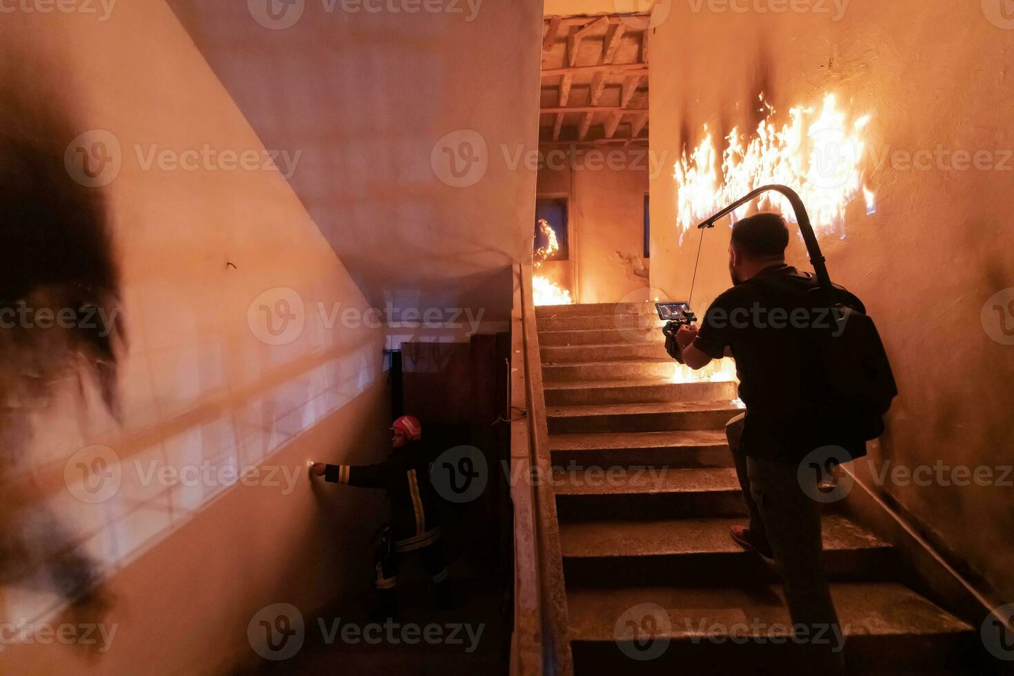 Brave Fireman Descends Stairs of a Burning Building and Holds Saved Girl in His Arms. Open fire. Cinematographer taking shoot with pro cinema camera and three-axis gimbal stabilization. low light photo