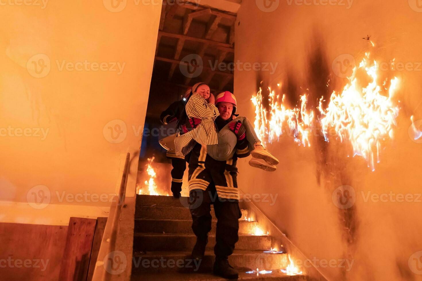 valiente bombero desciende escalera de un ardiente edificio y sostiene salvado niña en su brazos. abierto fuego y uno bombero en el antecedentes. foto