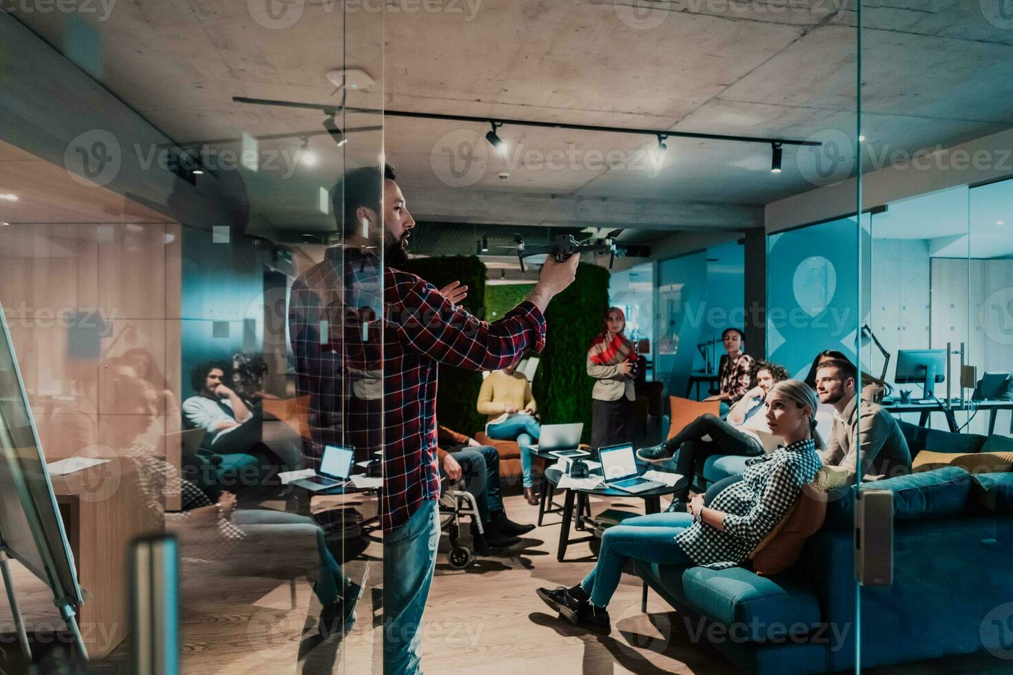 A bearded man in a modern office explaining to his young diverse team how a drone working photo