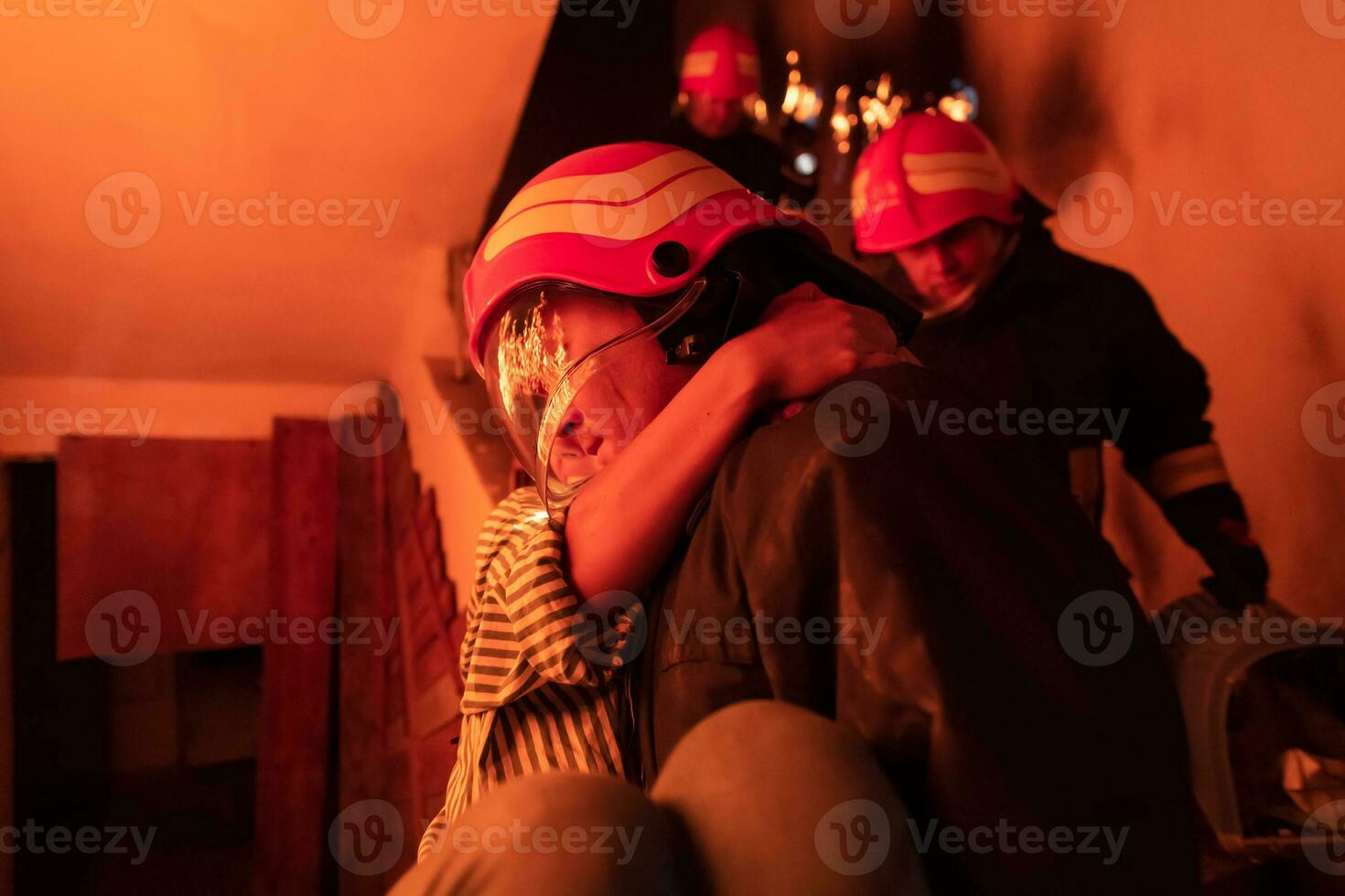 Brave Fireman Descends Stairs of a Burning Building and Holds Saved Girl in His Arms. Open fire and one Firefighter in the Background. photo