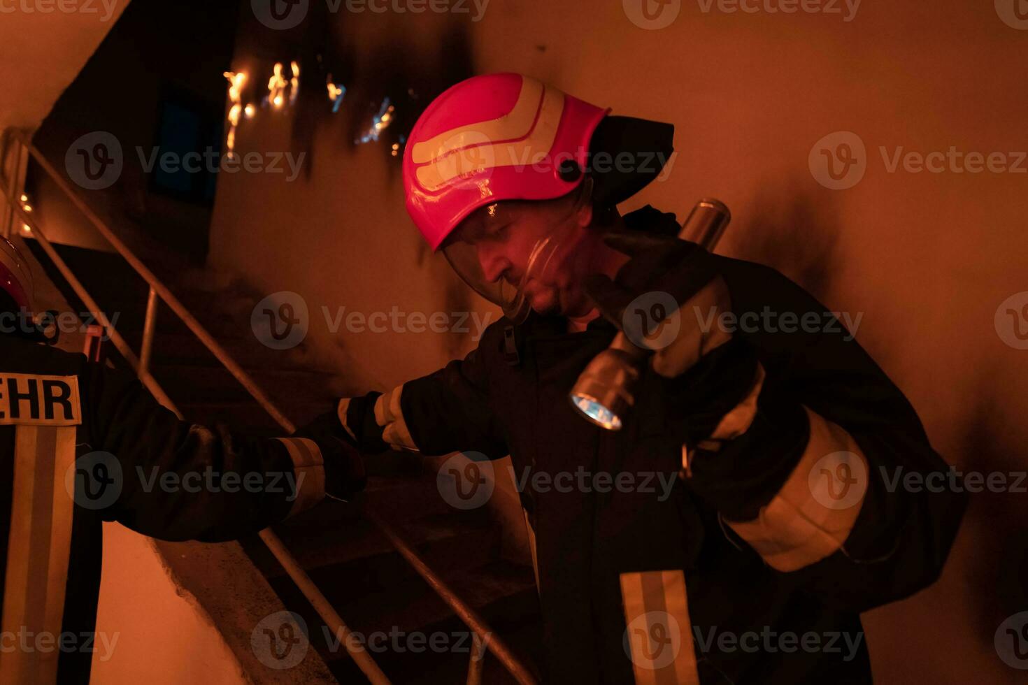 Brave Fireman Descends Stairs of a Burning Building and Holds Saved Girl in His Arms. Open fire and one Firefighter in the Background. photo