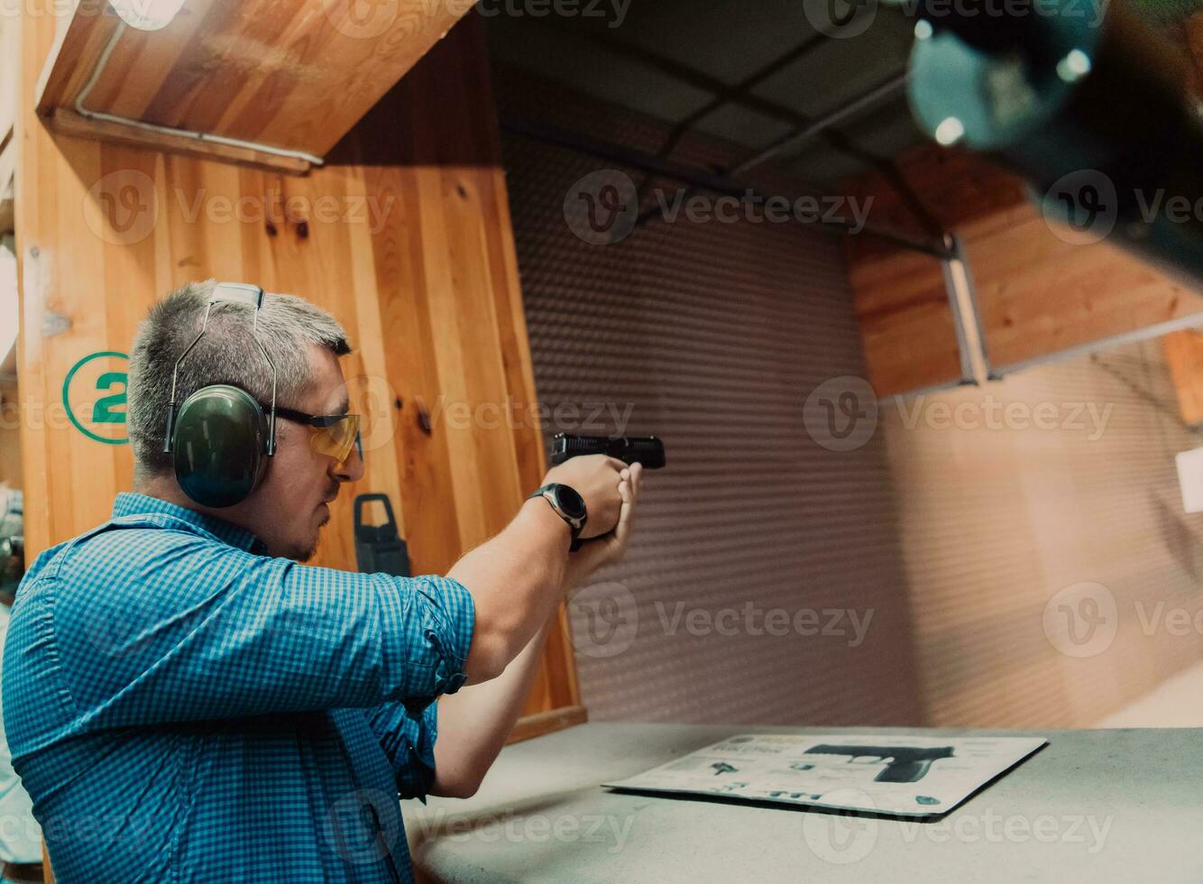 A man practices shooting a pistol in a shooting range while wearing protective headphones photo
