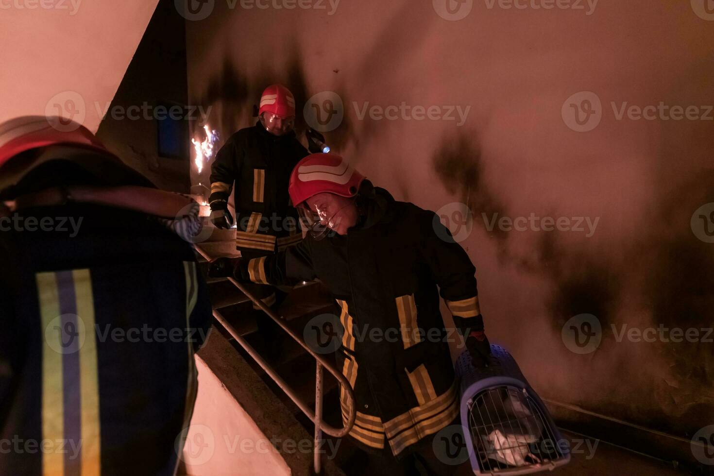 Brave Fireman Descends Stairs of a Burning Building and Holds Saved Girl in His Arms. Open fire and one Firefighter in the Background. photo