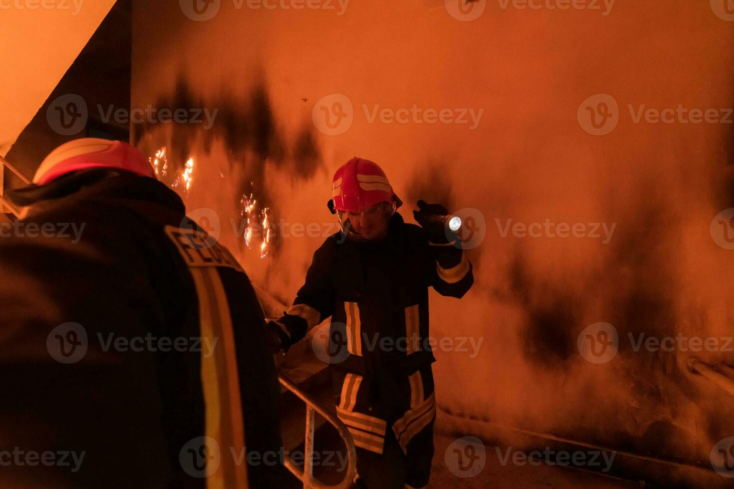 Brave Fireman Descends Stairs of a Burning Building and Holds Saved Girl in His Arms. Open fire and one Firefighter in the Background. photo