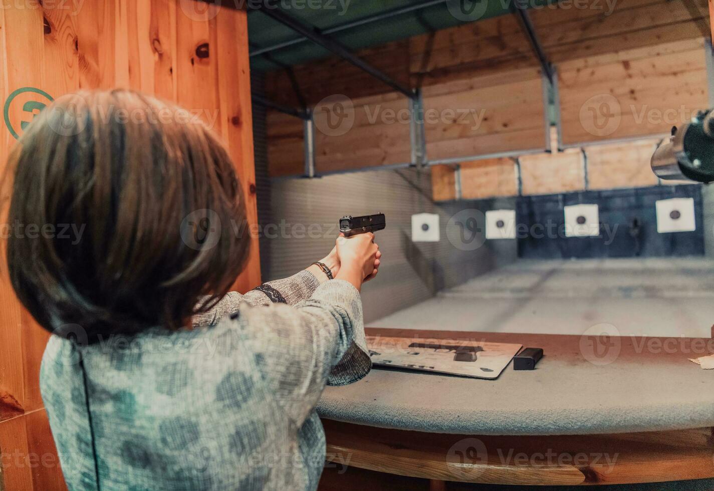 A woman practices shooting a pistol in a shooting range while wearing protective headphones photo