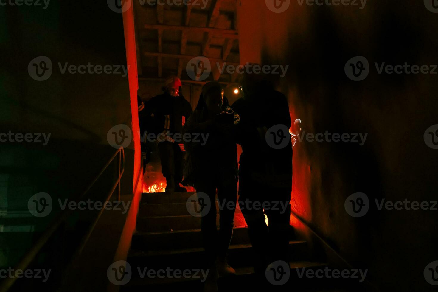 Brave Fireman Descends Stairs of a Burning Building and Holds Saved Girl in His Arms. Open fire and one Firefighter in the Background. photo