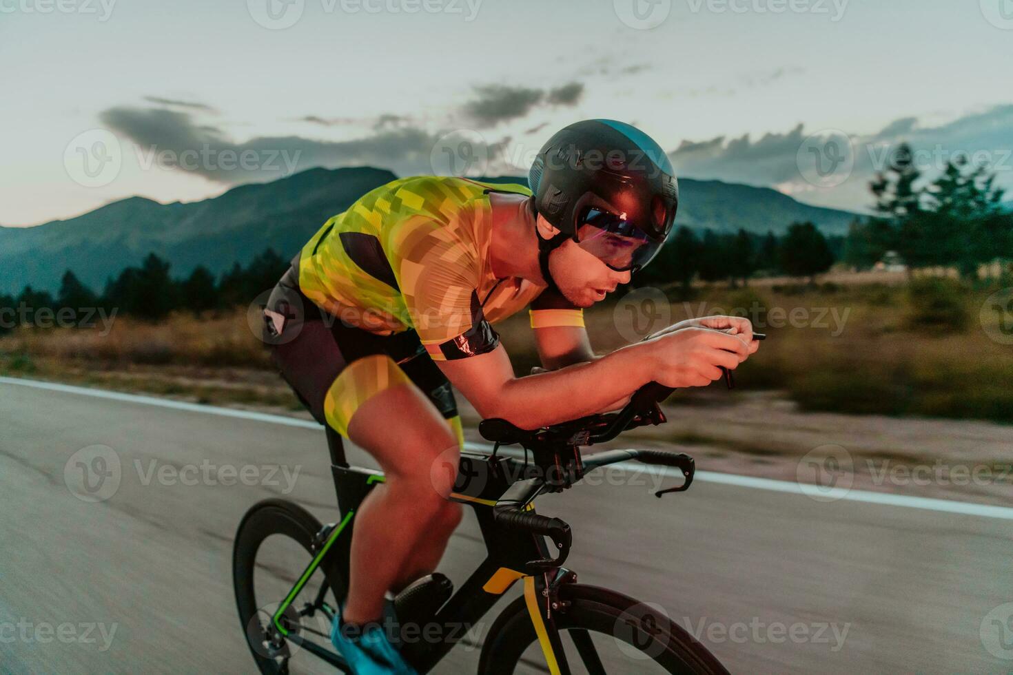 noche conducir. lleno longitud retrato de un activo triatleta en ropa de deporte y con un protector casco montando un bicicleta en noche tiempo.. selectivo atención foto