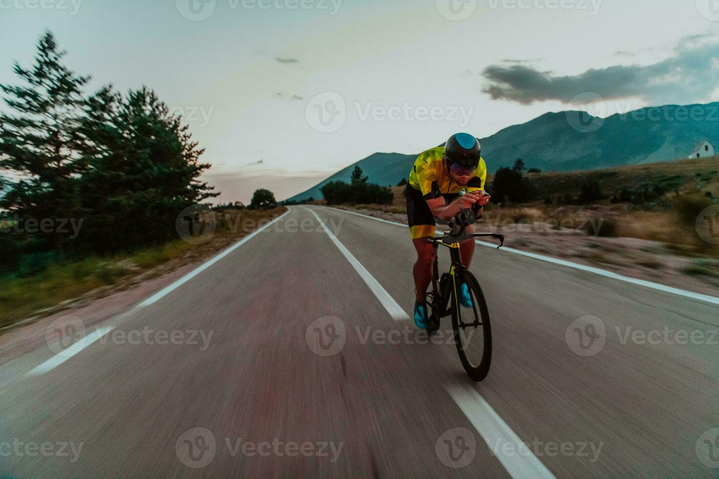 Night drive. Full length portrait of an active triathlete in sportswear and with a protective helmet riding a bicycle in night time.. Selective focus photo